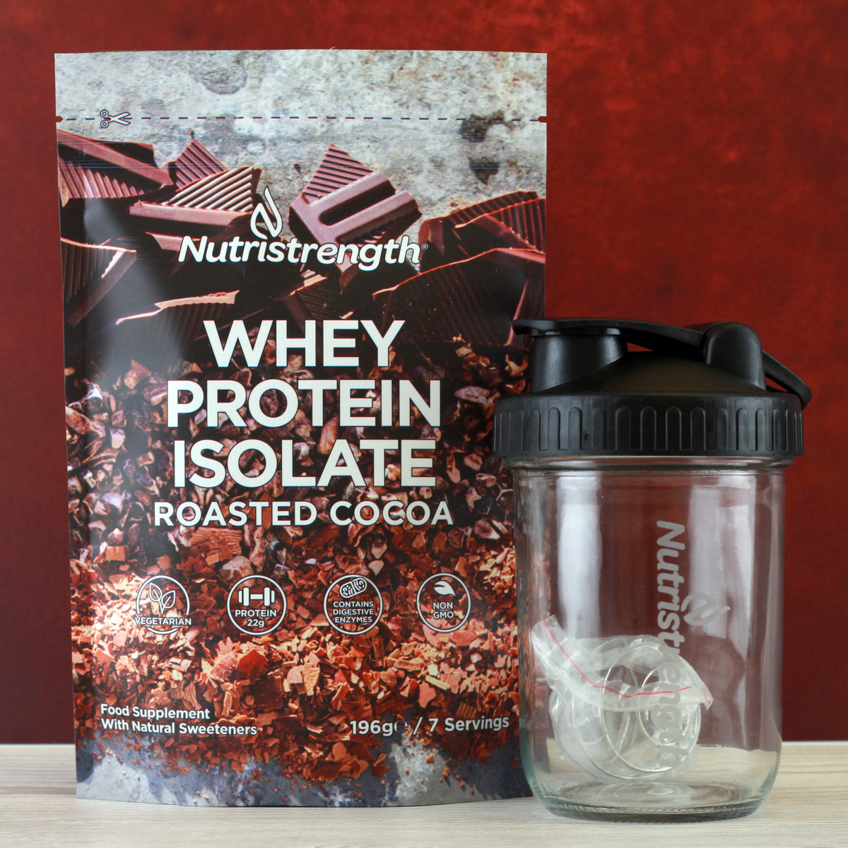 A package of Nutristrength Whey Protein Isolate in Roasted Cocoa flavor, accompanied by a clear glass shaker with the brand's logo.