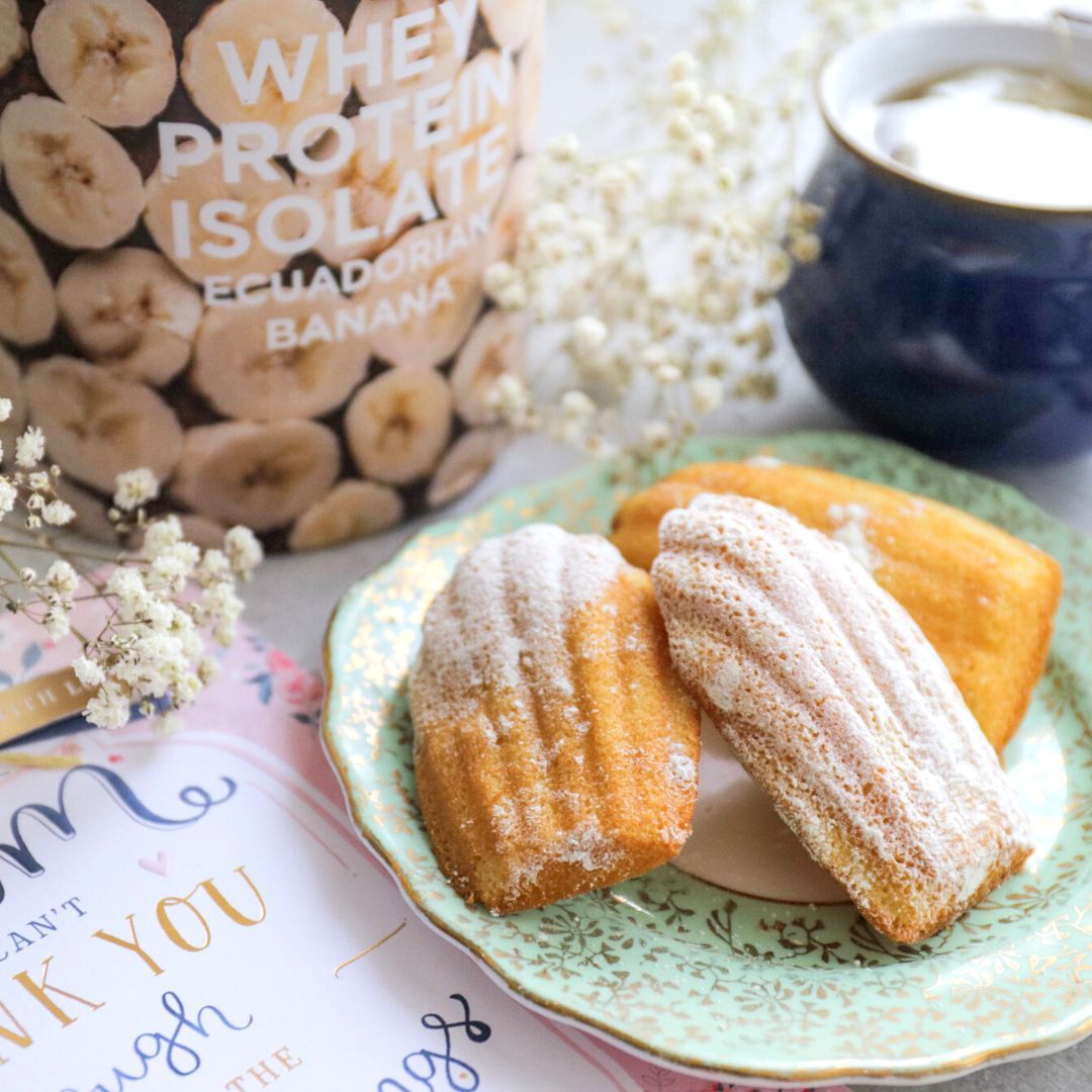 Mother's Day Protein Madelines made with Nutristrength's Banana Whey Protein Isolate in a cosy setting with a cup of tea, flowers and a Mother's Day card