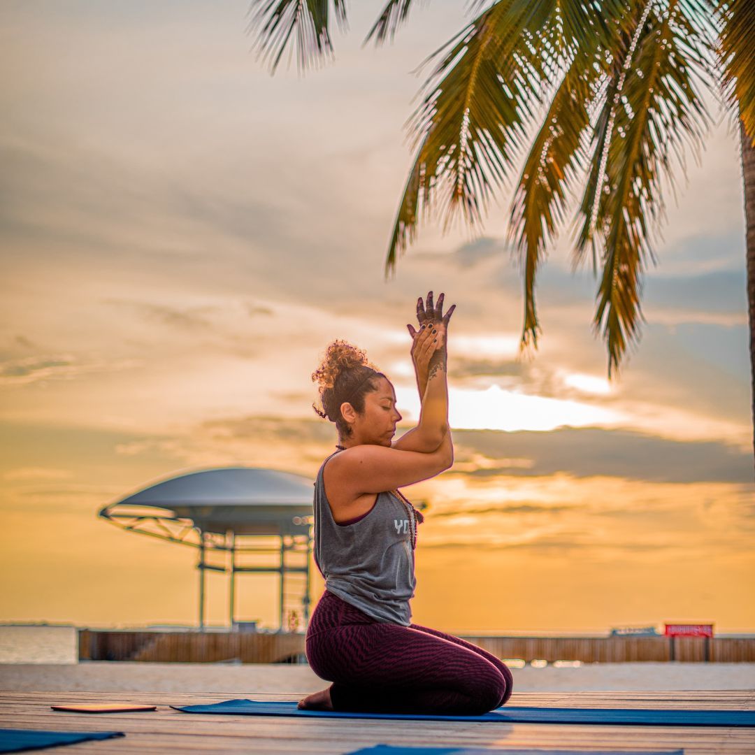 Lady doing yoga on the beach in front of a sunset